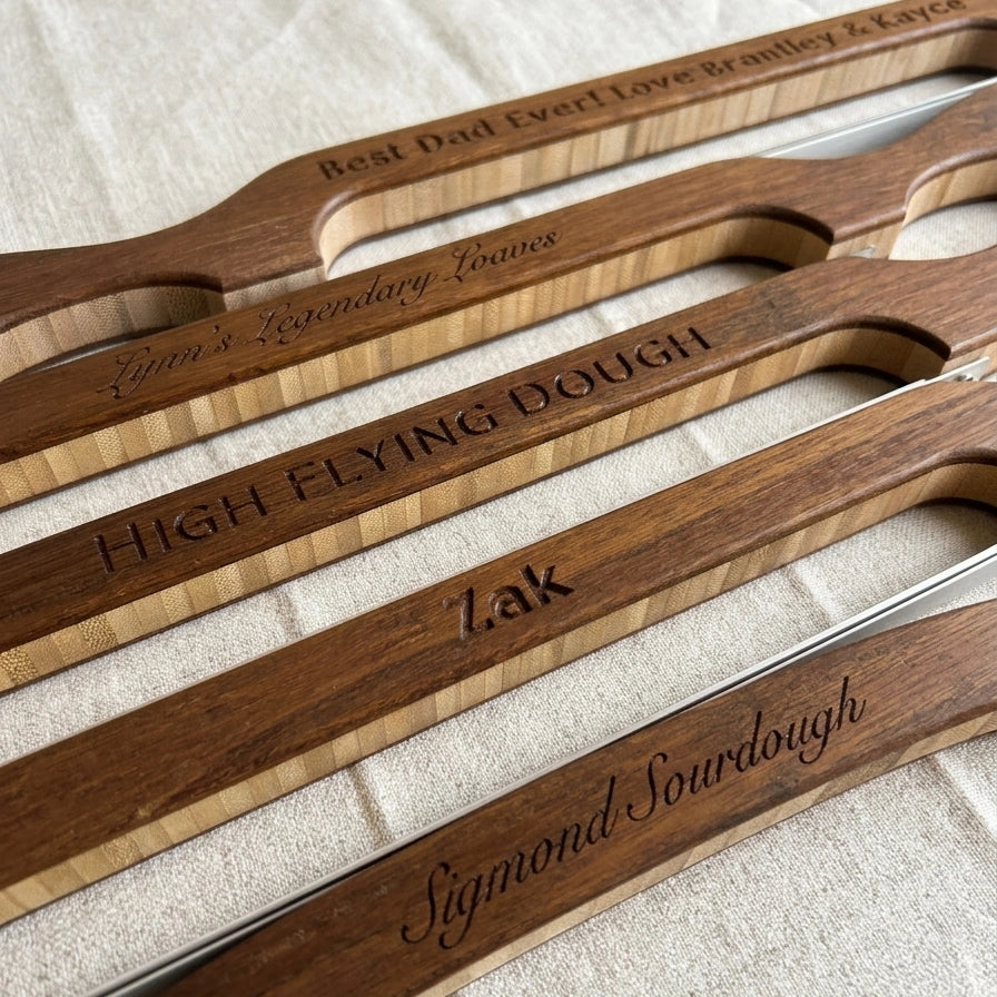 Personalized engraved sourdough bread knives by Loreto Studio displayed on natural linen, each handcrafted in solid wood with custom names and messages